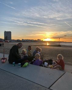 a group of people sitting next to each other on top of a sandy beach at sunset