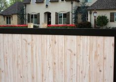 a wooden fence in front of a large house with red flowers on the bushes behind it