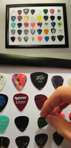 a person is pointing at a collection of guitar picks in front of a framed photo