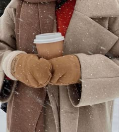 a woman in winter clothing holding a cup of coffee and wearing gloves with her arms crossed