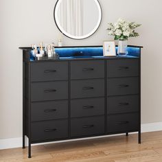 a black dresser with blue drawers in front of a round mirror on the wall above it