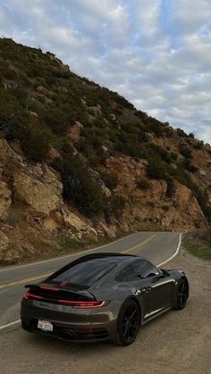 a black sports car is parked on the side of the road in front of a mountain