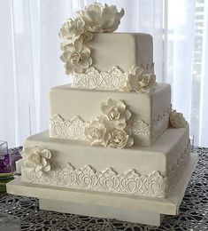 a three tiered wedding cake with white flowers on the side and lace around the edges