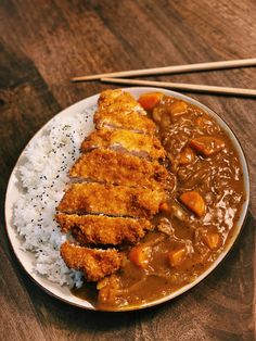 a white plate topped with rice and meat covered in gravy next to chopsticks