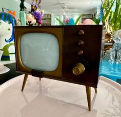 an old fashioned tv sitting on top of a white table next to glass vases