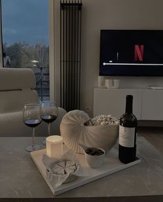 a wine bottle and two glasses on a tray in front of a flat screen tv