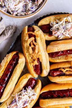 several hot dogs with toppings in buns on a tray next to a bowl of coleslaw