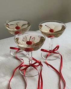 three martini glasses with cherries in them on a white tablecloth, tied with red ribbon