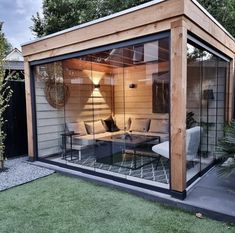 an outdoor living area with glass walls and wooden structure, surrounded by green lawning