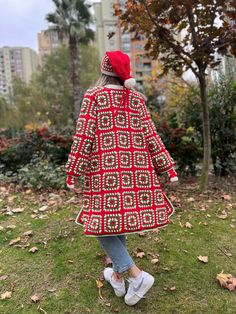 a woman in a red and white coat is standing on the grass with her back to the camera