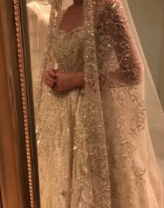 a woman in a wedding dress standing next to a mirror with her veil draped over her head