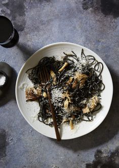 a white plate topped with pasta and meat next to a glass of wine on top of a table