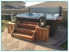 a hot tub sitting on top of a stone patio next to a wooden table and steps