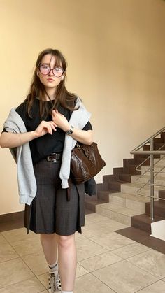 a woman standing in front of some stairs with her hand on her purse and looking at the camera