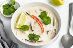 a white bowl filled with soup and garnished with cilantro, red pepper, green leaves