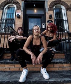 three young women sitting on the steps in front of a brick building with black wrought iron railings