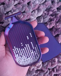 a person holding a purple comb with white beads on it and a blue holder in their hand