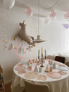 a white table topped with plates and cups filled with cake next to balloons hanging from the ceiling