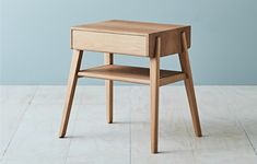 a small wooden table with one drawer on the bottom and two shelves below it, against a blue wall