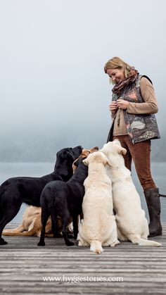 a woman standing next to several dogs on a dock