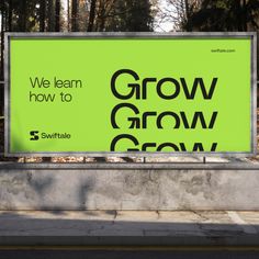 a large green sign sitting on the side of a road in front of some trees