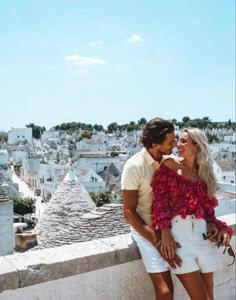 a man and woman standing next to each other on top of a roof with buildings in the background