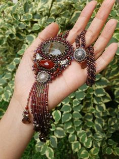 a woman's hand holding a red beaded bracelet with stones and beads on it