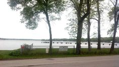 the road is lined with trees next to the water and a bridge in the distance