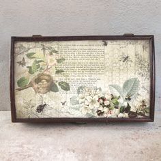 an old frame with flowers and bugs on it is sitting next to a white wall