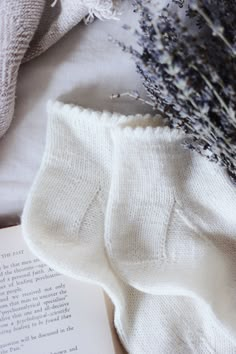 an open book and some lavender flowers on a white sheet with a knitted cover