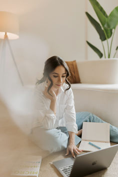 a woman is sitting on the floor working on her laptop