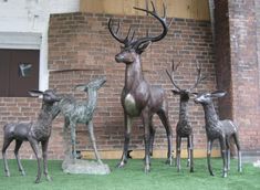 four deer statues are standing in front of a brick building with grass on the ground