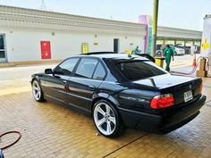 a black car parked in front of a gas station with people standing around the pump