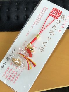 a red and gold keychain with chinese writing on the front is attached to a plastic package