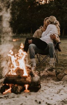 a man and woman sitting in chairs next to a campfire with their arms around each other