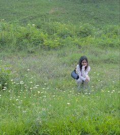 a woman kneeling in the grass with a suitcase