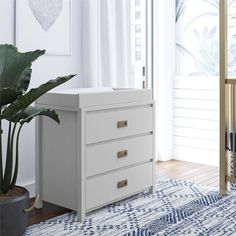 a white dresser sitting on top of a wooden floor next to a potted plant