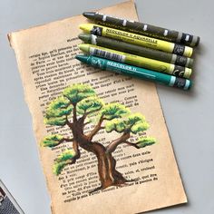 some crayons are sitting on top of an old book with a tree drawn on it