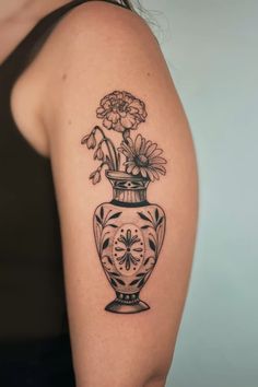 a woman's arm with flowers in a vase tattoo on the left side of her shoulder