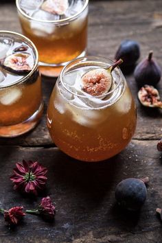 two glasses filled with liquid next to figs and flowers on a wooden table top