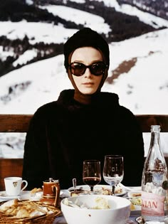 a woman wearing sunglasses sitting at a table with wine glasses and food in front of her