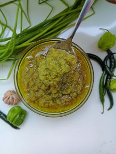 a small bowl filled with green food next to some flowers and herbs on a white surface