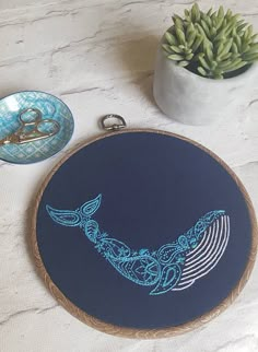 a blue whale embroidered on a wooden hoop next to some scissors and a bowl with succulents