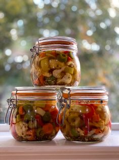 four jars filled with pickles and vegetables on top of a window sill next to a tree