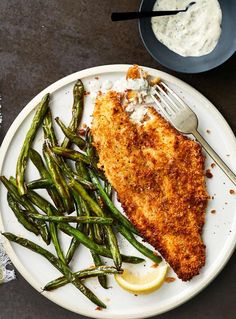 a white plate topped with fish and green beans next to a bowl of ranch dressing