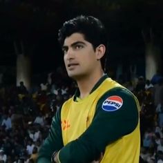 a man standing in front of a crowd wearing a green and yellow shirt with his arms crossed