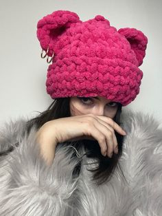 a woman wearing a pink knitted hat with ears and claws on her head is posing for the camera