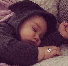 a baby sleeping on top of a bed wearing a hoodie and holding a pacifier