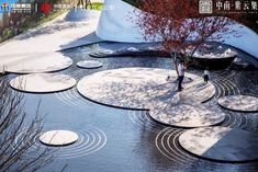 an outdoor pond with stepping stones and trees in the water, surrounded by snow - covered rocks