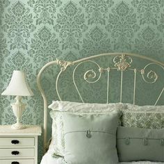 a white bed topped with pillows next to a night stand and lamp on top of a dresser